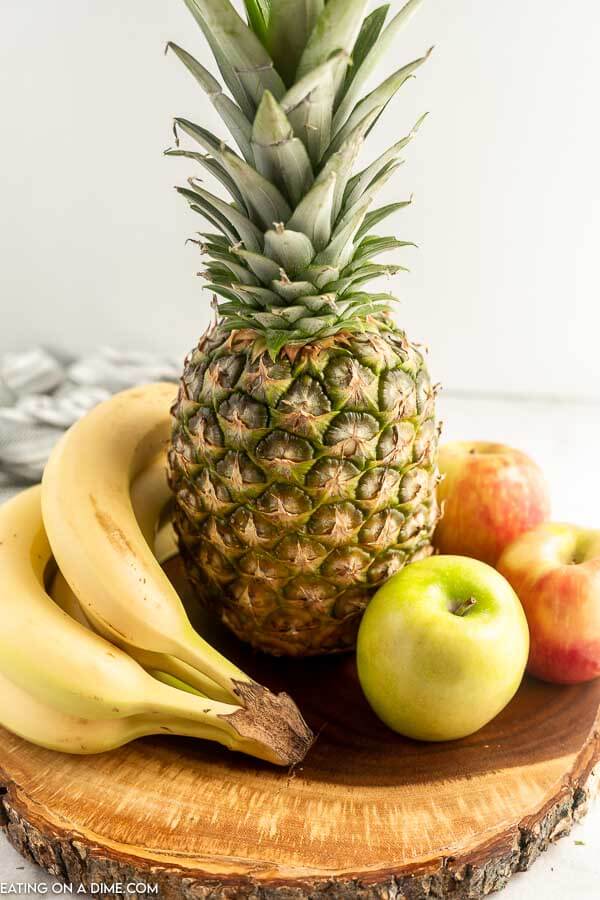 Close up image of a pineapple, banana, and applies on a wood stand. 