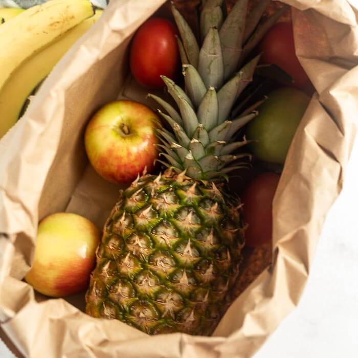 Close up image of a pineapple in a paper bag with apples. 