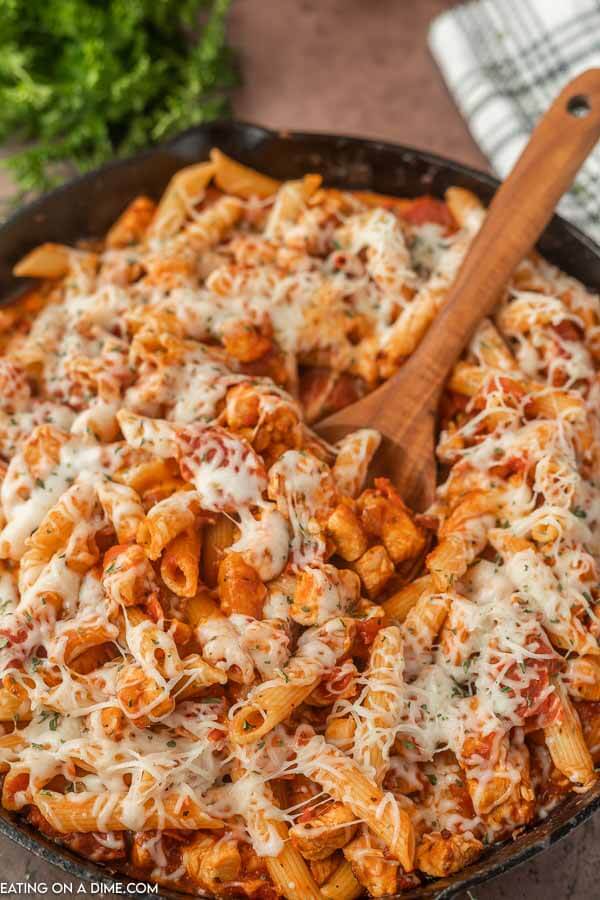 Close up image of Chicken Pepperoni Pasta in an iron skillet with a wooden spoon. 