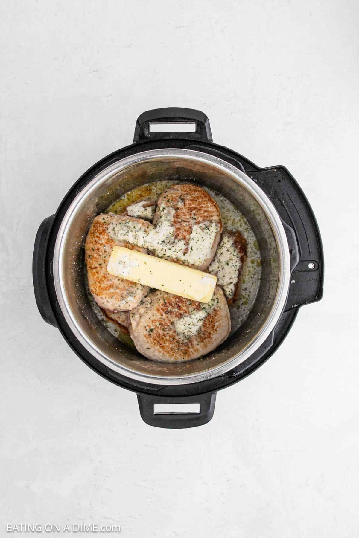 Seared pork chops in the instant pot topped with ranch seasoning and a stick of butter.