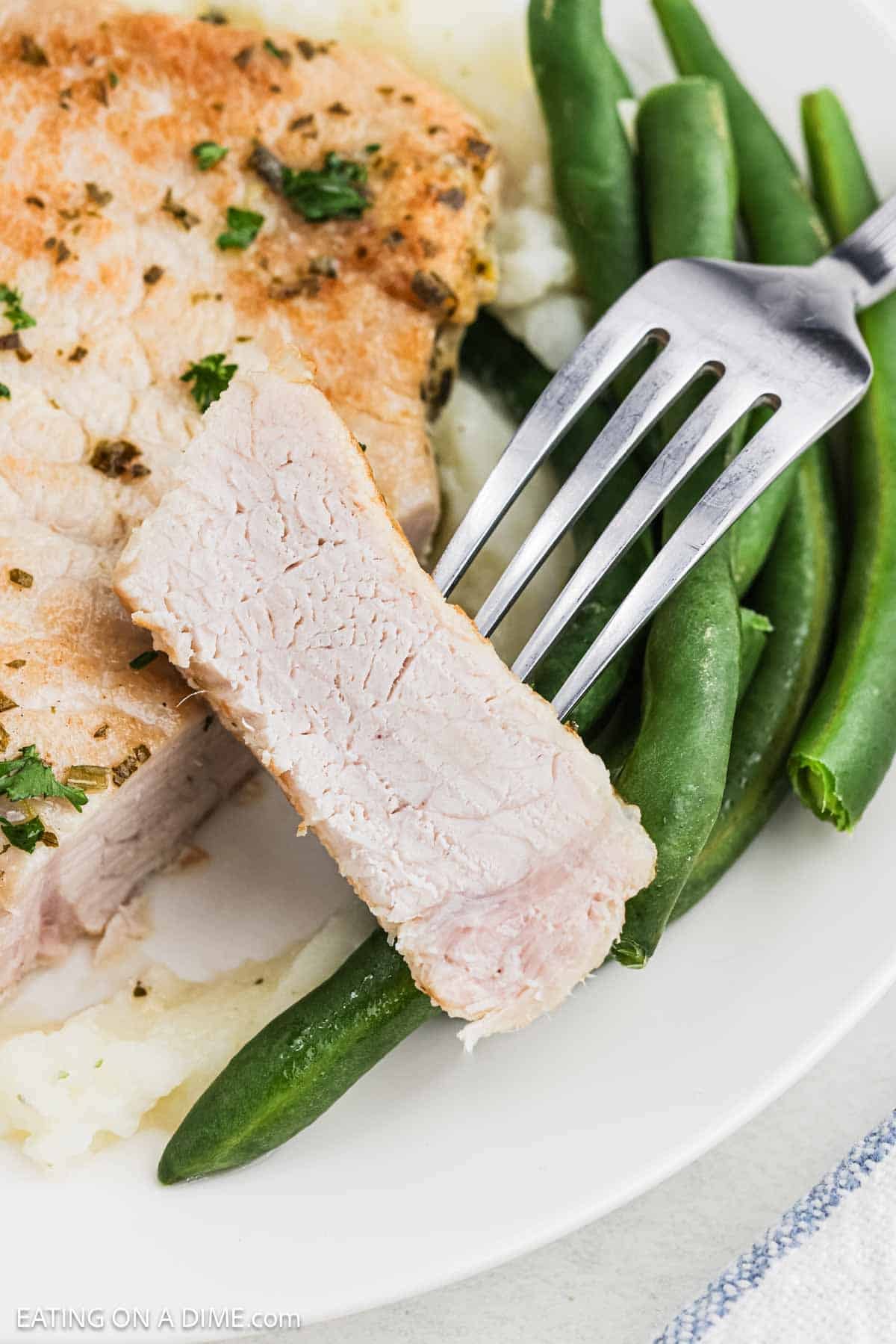 Instant Pot pork chops with a bite on the fork with a side of green beans.