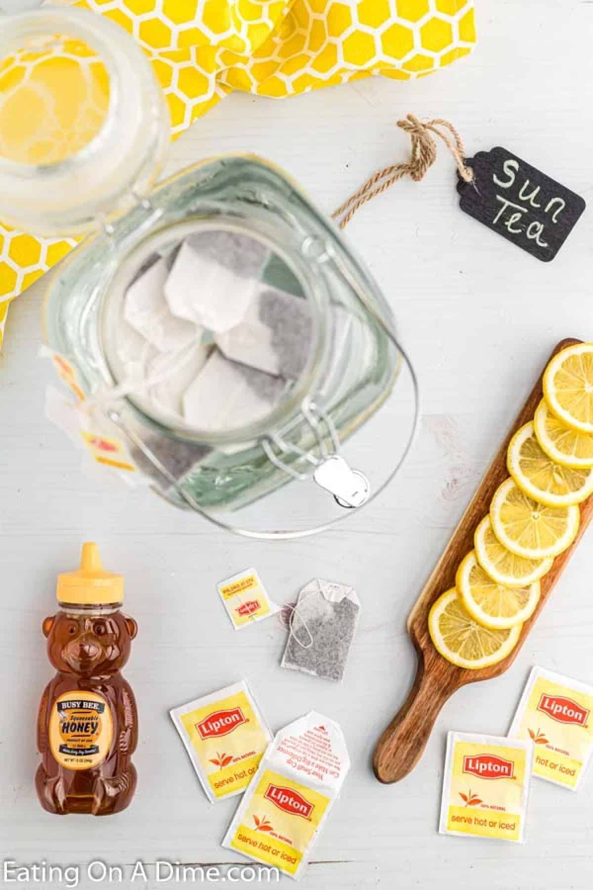 Tea bags in a large pitcher with slices of lemon, honey and tea bags on the side