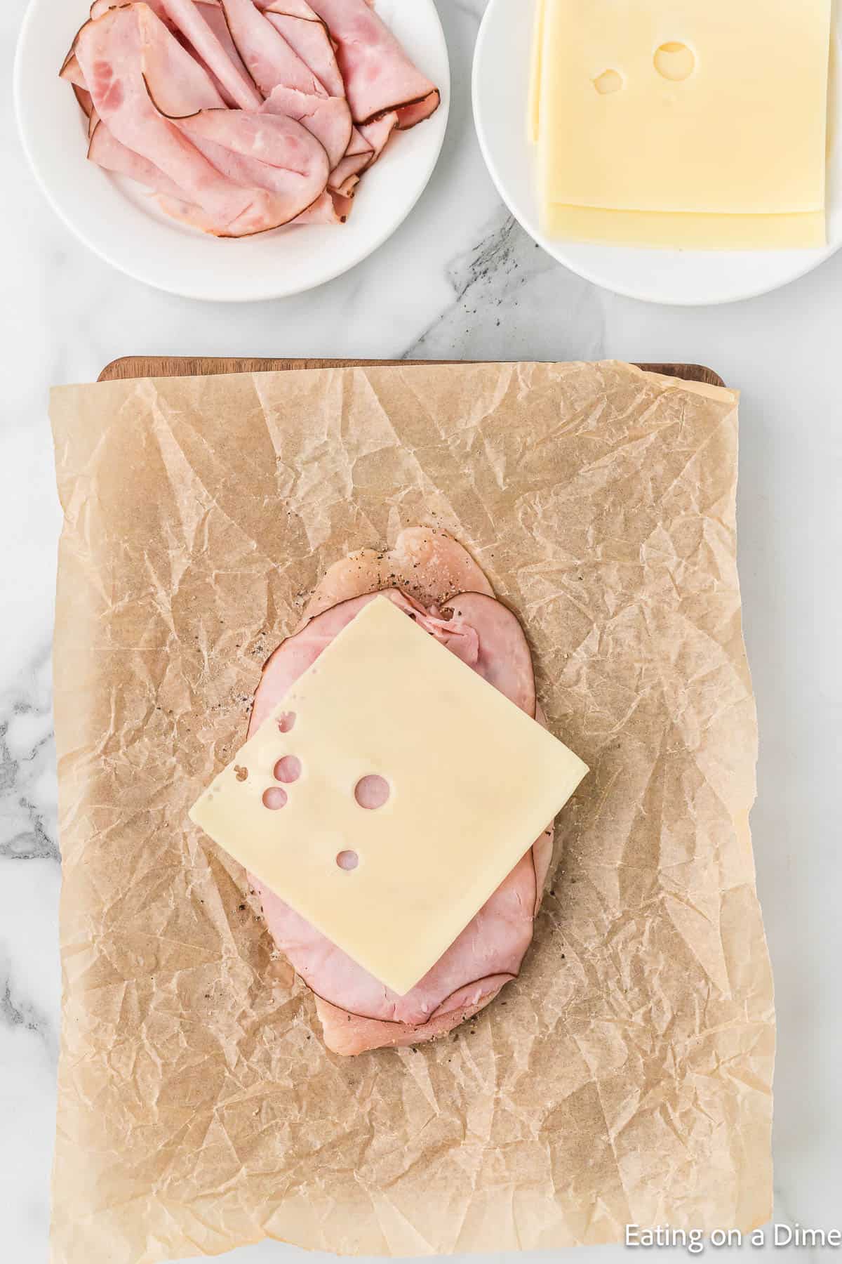 Topping the chicken breast with ham and slice cheese with a plate of ham and slice cheese on the side
