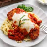 A serving of chicken parmesan on a plate over spaghetti.