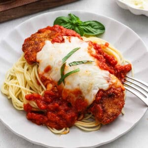 A serving of chicken parmesan on a plate over spaghetti.