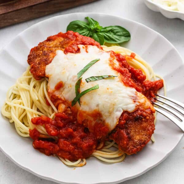A serving of chicken parmesan on a plate over spaghetti.