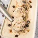 A close-up of a Chunky Monkey Ice Cream container with scoops on top, featuring chocolate chunks and nuts, with an ice cream scooper resting in the container.