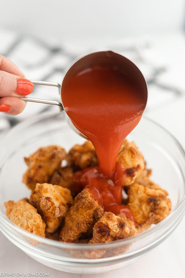 Buffalo sauce is being poured over chicken wings in a clear bowl