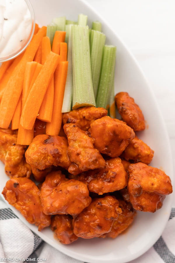 Close up image of boneless chicken wings and carrots and celery on a white plate. 