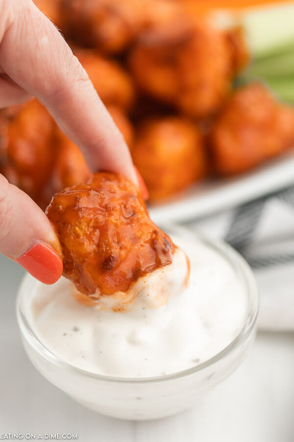 Close up image of boneless chicken wings being dipped in ranch. 