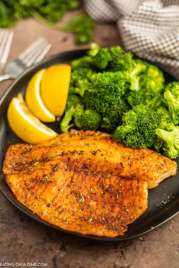 Air fryer tilapia on a plate with broccoli and lemon slices. 