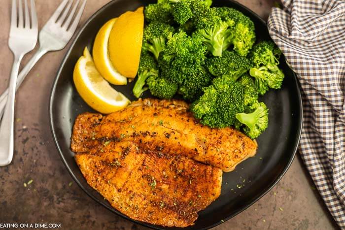 Air fryer tilapia on a plate with broccoli and lemon slices. 