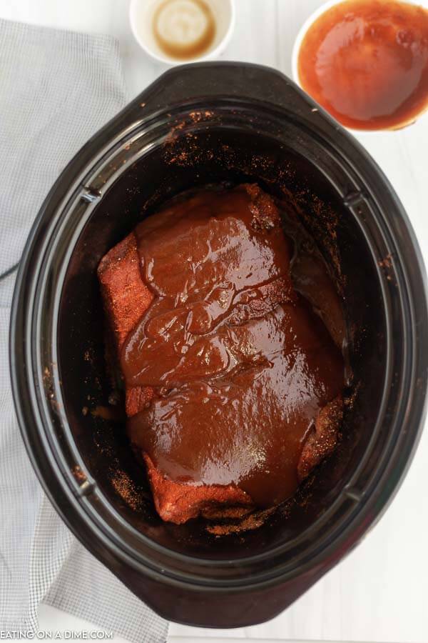Uncooked brisket in a crock pot with BBQ sauce poured over top. 