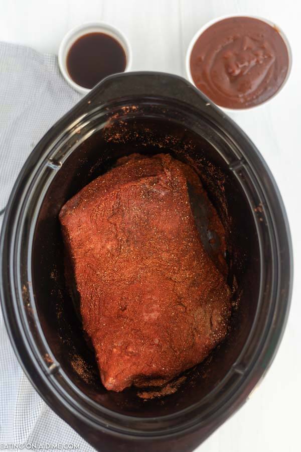 Uncooked brisket in a crock pot with seasoning sprinkled on top. 