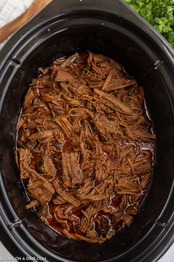 Learn how to make Crock Pot Brisket Recipe that is so tender it falls apart. The flavor from being slow cooked all day is amazing and the recipe is so easy. Close up image of shredded beef brisket in a crock pot