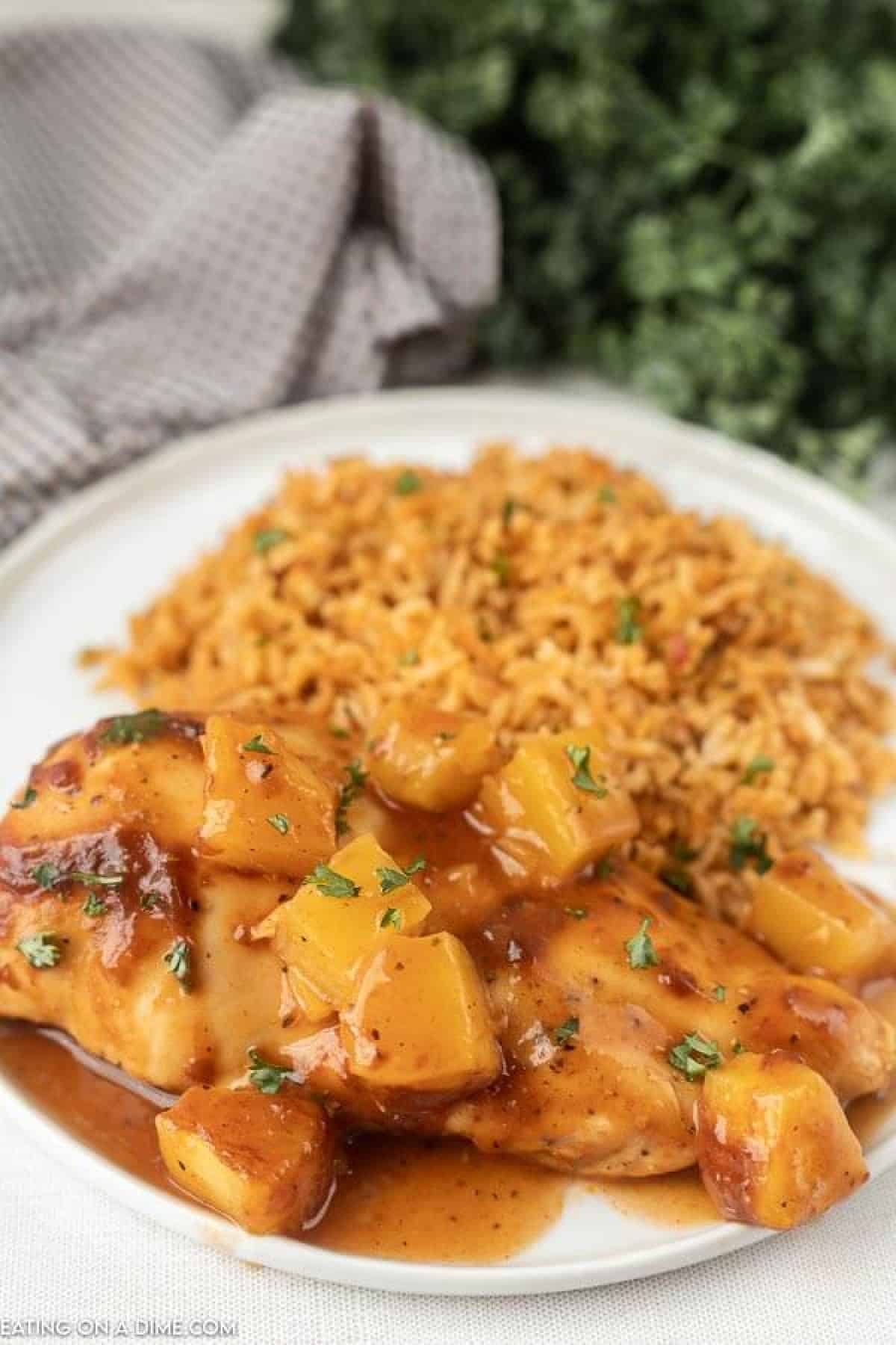 Baked Pineapple BBQ chicken recipe is the perfect meal idea and only requires 3 ingredients. It is so easy but tastes like you spent all day cooking. Close up image of chicken on a plate with a side of rice.