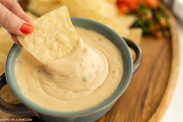 Close up image of queso in a bowl with a side of chips and a chip being dipped in the queso