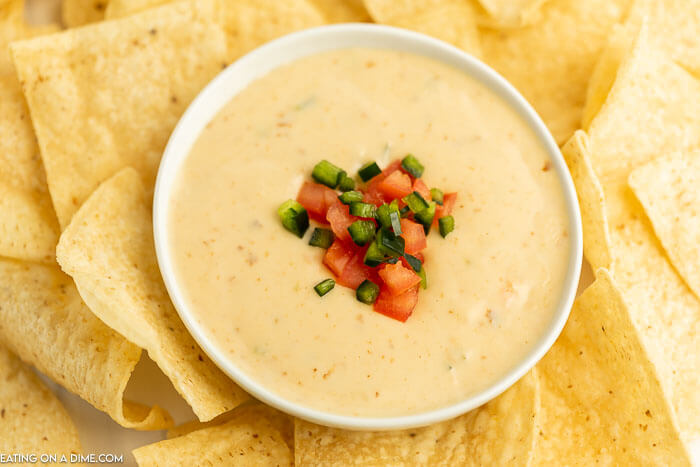 Close up image of queso in a bowl with a side of chips topped with tomato and jalapeno