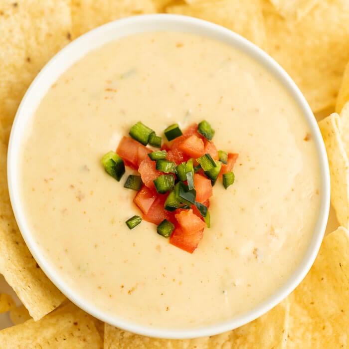 Close up image of queso in a bowl with a side of chips topped with tomato and jalapeno