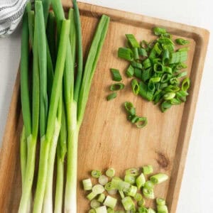 A wooden cutting board with whole green onions on the left and sliced green onions in small and large pieces on the right—perfect for discovering The Best Green Onion Substitutes for your next recipe.