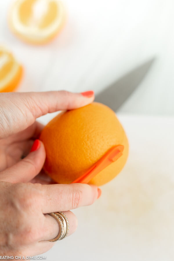 Close up image of using a orange peeler to begin peeling an orange. 