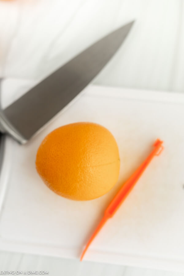 Close up image of an orange on a cutting board with an orange peeler and a knife. 