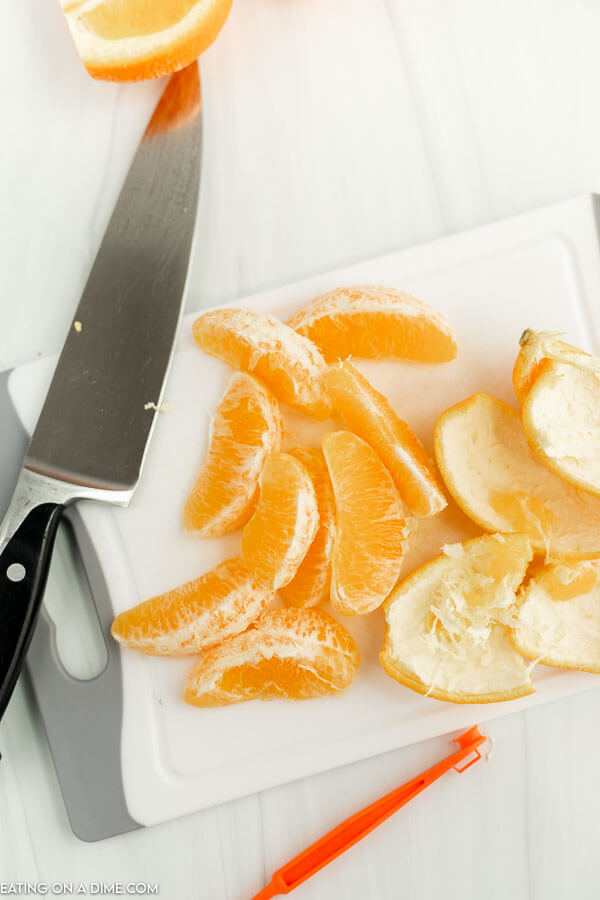 Close up image of orange slices on a cutting board with a knife and a orange peeler. 