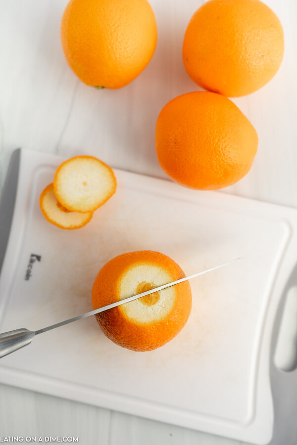 Close up image of cutting the orange in half with a knife on a cutting board. 