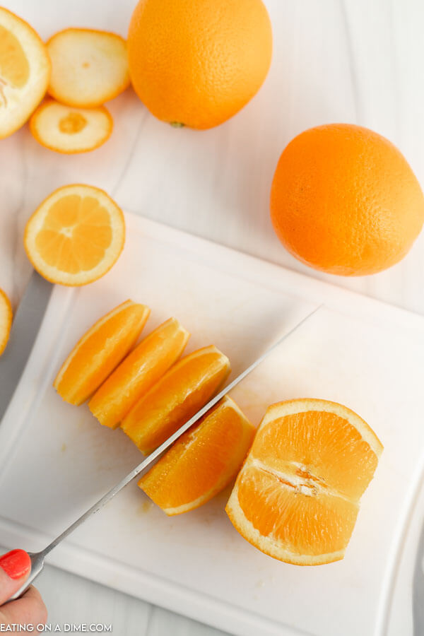 Close up image of cutting orange slices with a knife on a cutting board. 