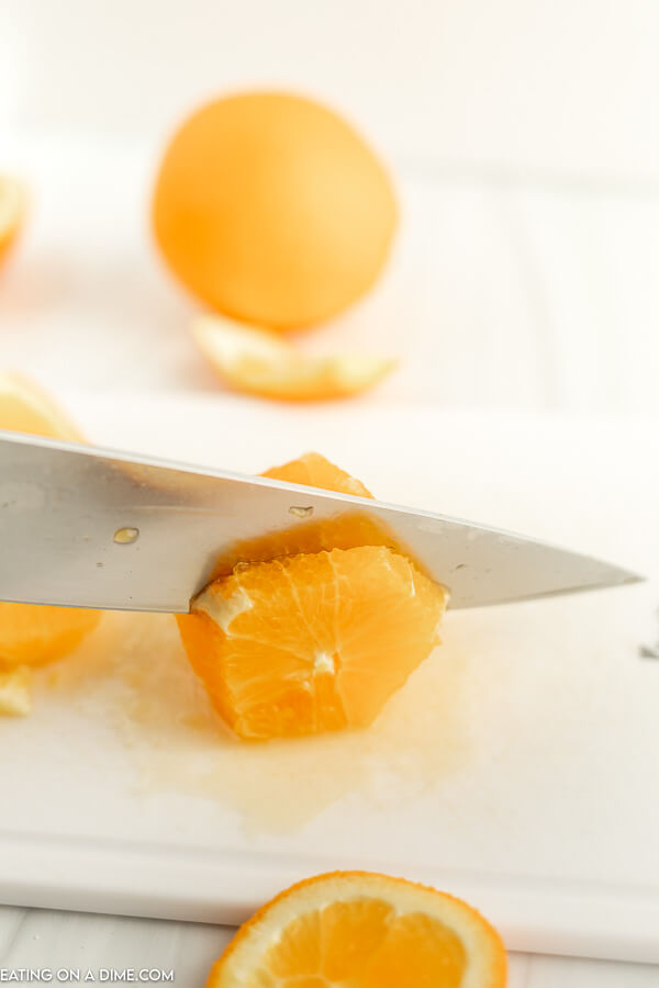 Close up image of a orange slices being cut with a knife on a cutting board. 