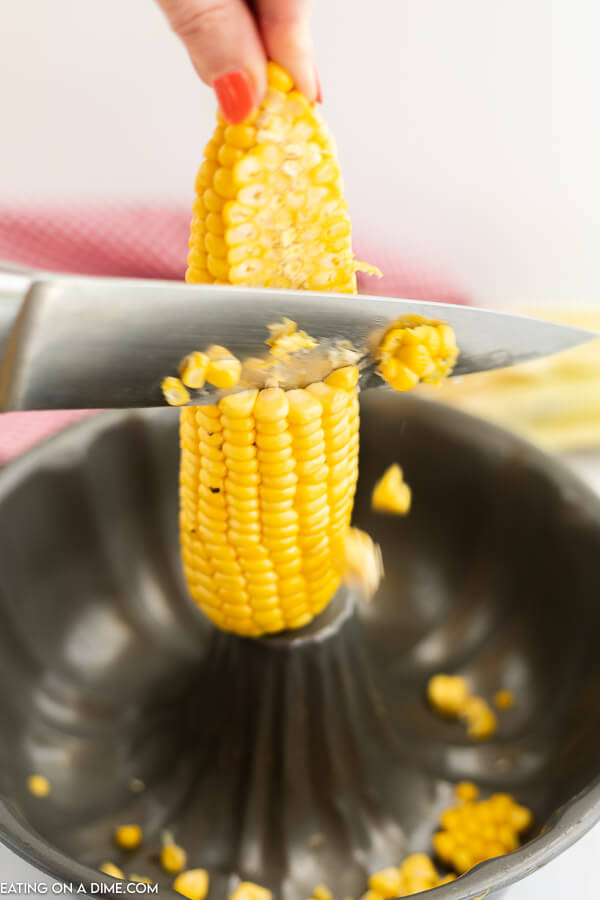 Close up image of kernels being cut off the cob into a bundt pan. 