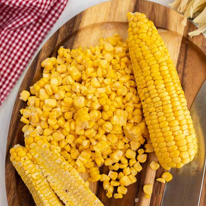 Close up image of corn on the cob with kernels on a cutting board with a knife. 
