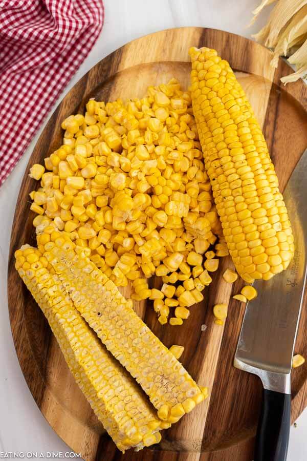 Close up image of corn on the cob with kernels on a cutting board with a knife. 
