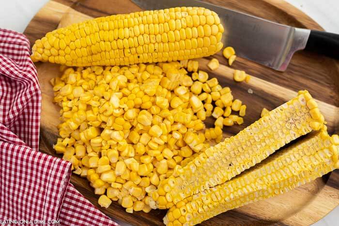 Close up image of corn on the cob with kernels on a cutting board with a knife. 