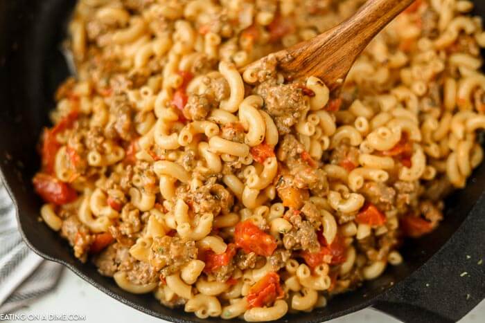 close up image of sausage mac and cheese and a skillet with a wooden spoon. 