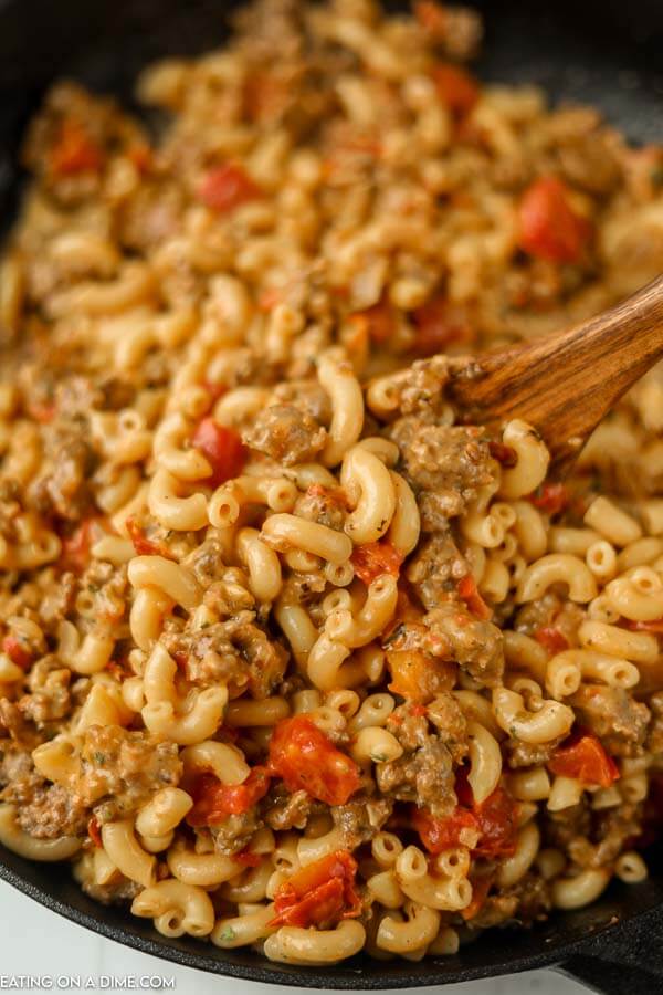 close up image of sausage mac and cheese and a skillet with a wooden spoon