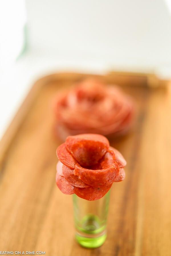 A pepperoni rose on a shot glass sitting on a board. 