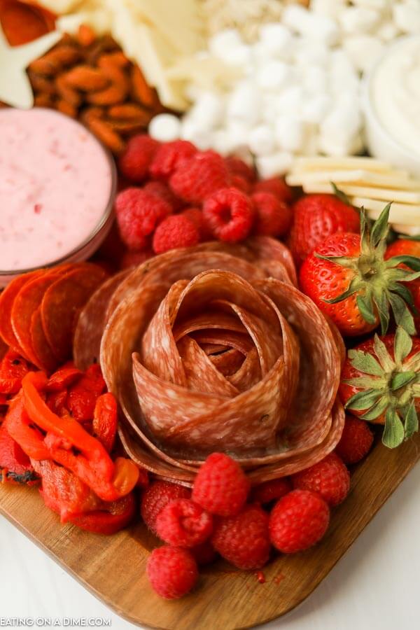A close up image of a charcuterie board with a salami rose with fruits pepperoni cheese and dips