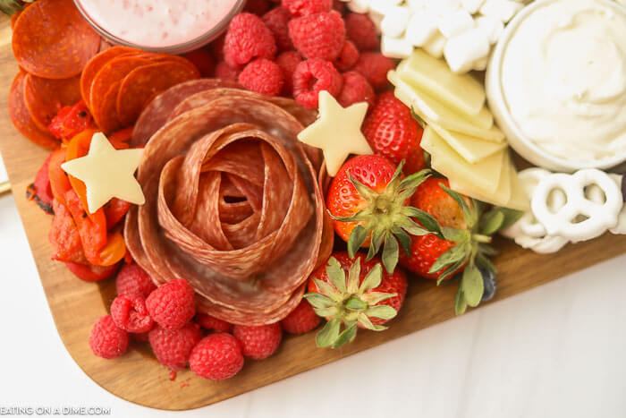 A close up image of a charcuterie board with a salami rose with fruits pepperoni cheese and dips