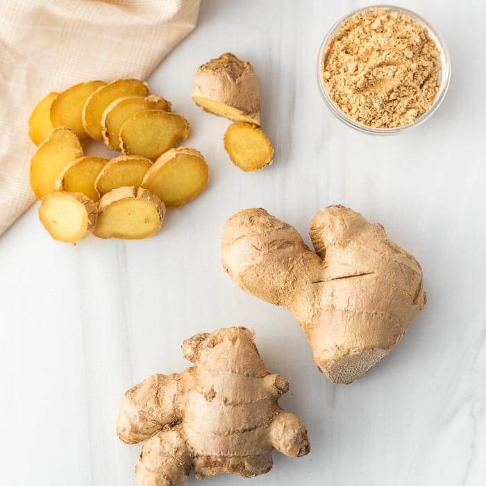 Close image of a ginger root, slice ginger and a bowl of ground ginger. 