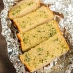 Four slices of grilled garlic bread, infused with herbs, rest enticingly on crinkled aluminum foil.
