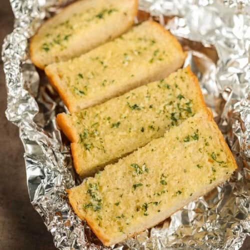 Four slices of grilled garlic bread, infused with herbs, rest enticingly on crinkled aluminum foil.
