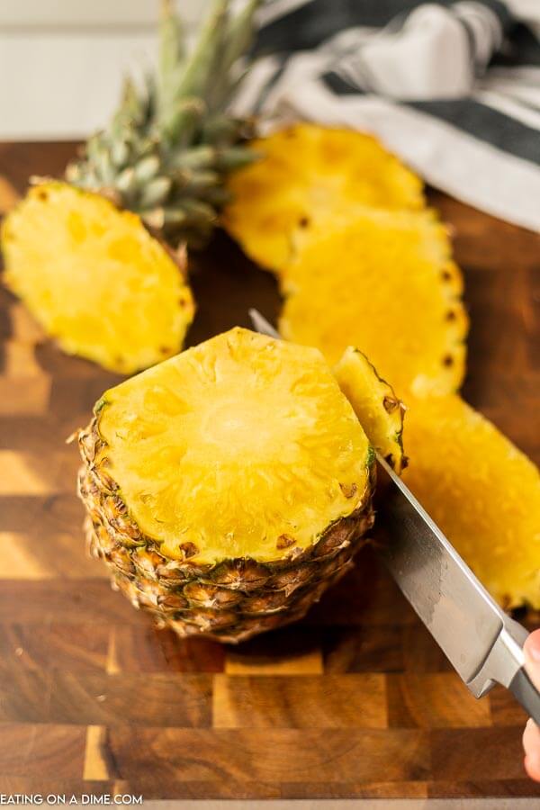 Cutting the skin off the pineapple with a knife. 
