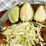 How to Cut Cabbage: Chopped green cabbage sits on a wooden cutting board, accompanied by three perfectly sliced wedges and a sharp knife. Nearby, a checkered cloth adds a touch of charm to the scene.