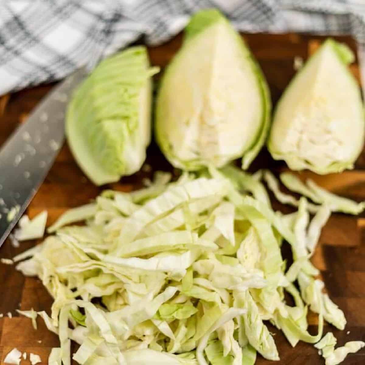 How to Cut Cabbage: Chopped green cabbage sits on a wooden cutting board, accompanied by three perfectly sliced wedges and a sharp knife. Nearby, a checkered cloth adds a touch of charm to the scene.