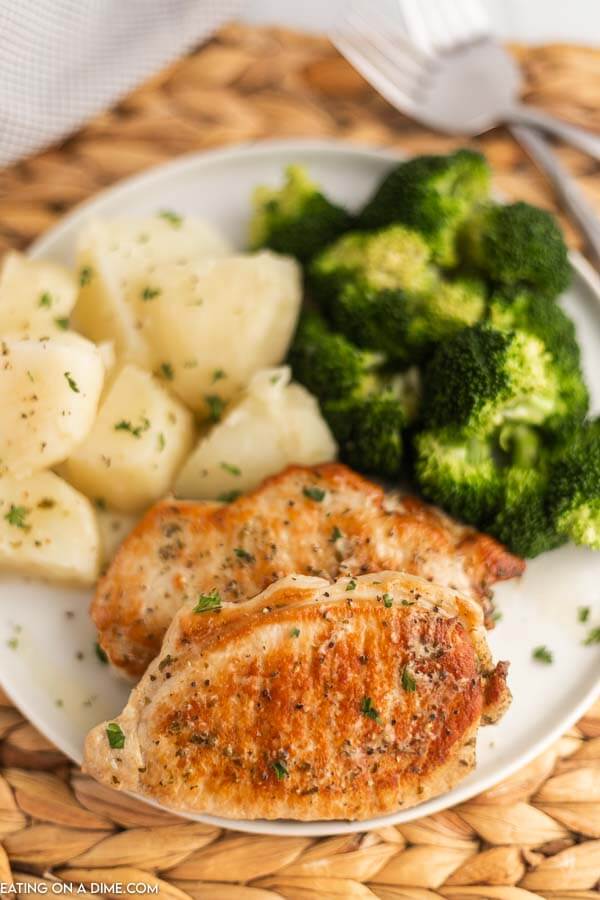 Close up image of pork chops on a white plate with a side of potatoes and broccoli. 