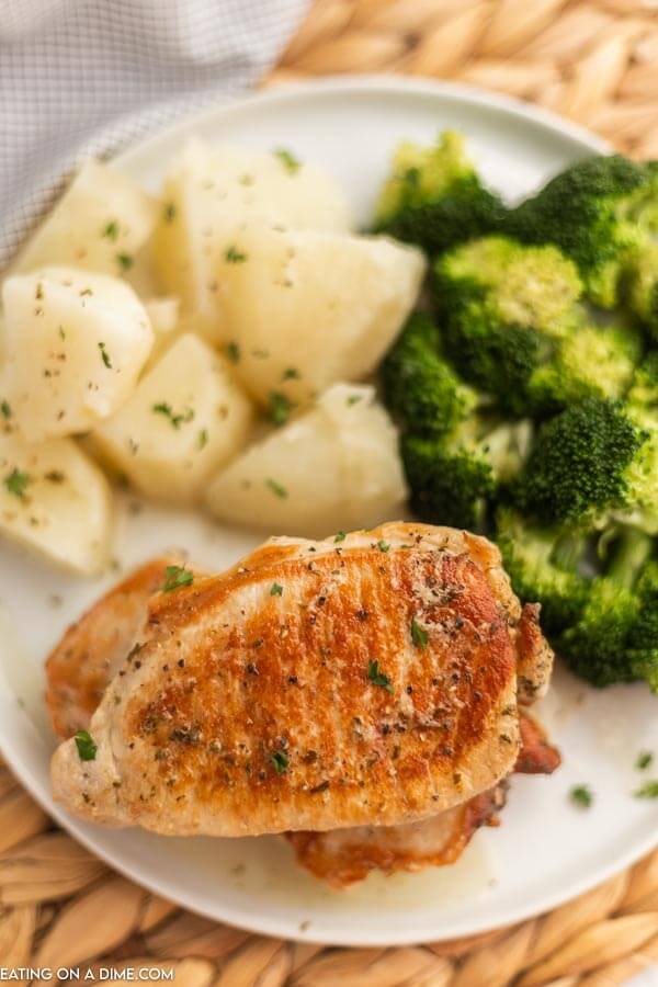 Close up image of pork chops on a white plate with a side of potatoes and broccoli. 