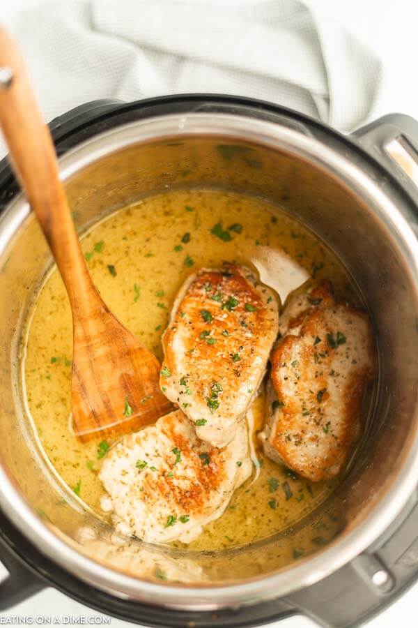 Close up image of pork chops in instant pot with a wooden spoon. 