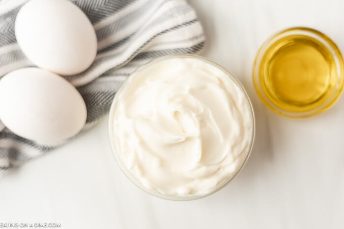 Close up image of Mayonnaise in a bowl with a side of oil and two eggs. 