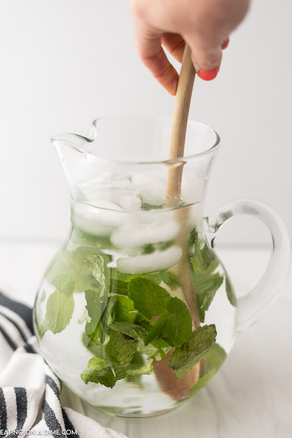 Mint water in glass pitcher being stirred. 